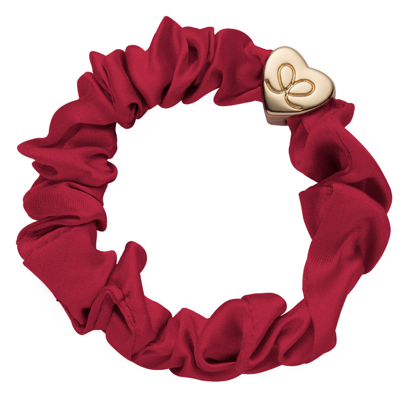 The ByEloise Silk Scrunchie in Burgundy Red, featuring gathered silk and a Gold Heart charm, adds an elegant touch to any look.