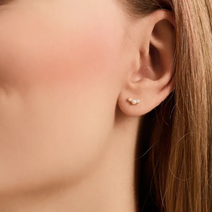 Close-up of a woman with straight, light brown hair wearing Pernille Corydon’s Ocean Pearl Earsticks Earrings in Gold—an elegant, delicate design featuring two tiny pearls for a nature-inspired look.