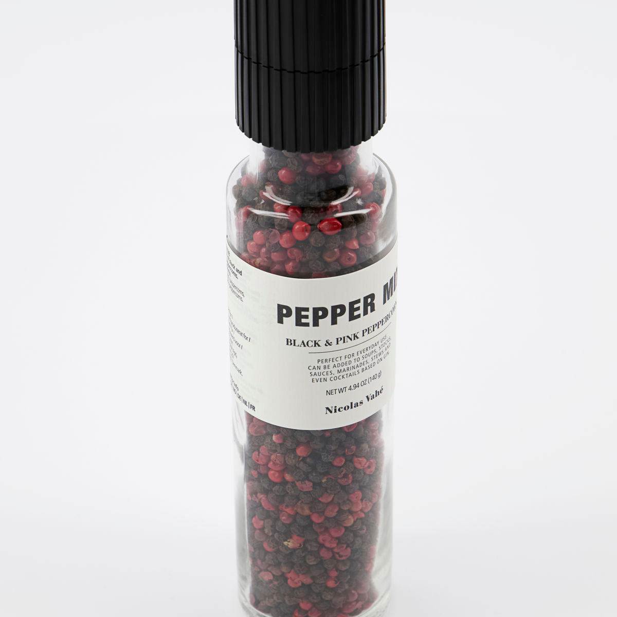 A clear glass grinder bottle from Nicolas Vahe, filled with black and pink peppercorns, features a ceramic grinder top and a white label reading PEPPER MIX BLACK & PINK PEPPERCORNS. Product name: Pepper Mix Grinder w. Black & Pink peppercorns.