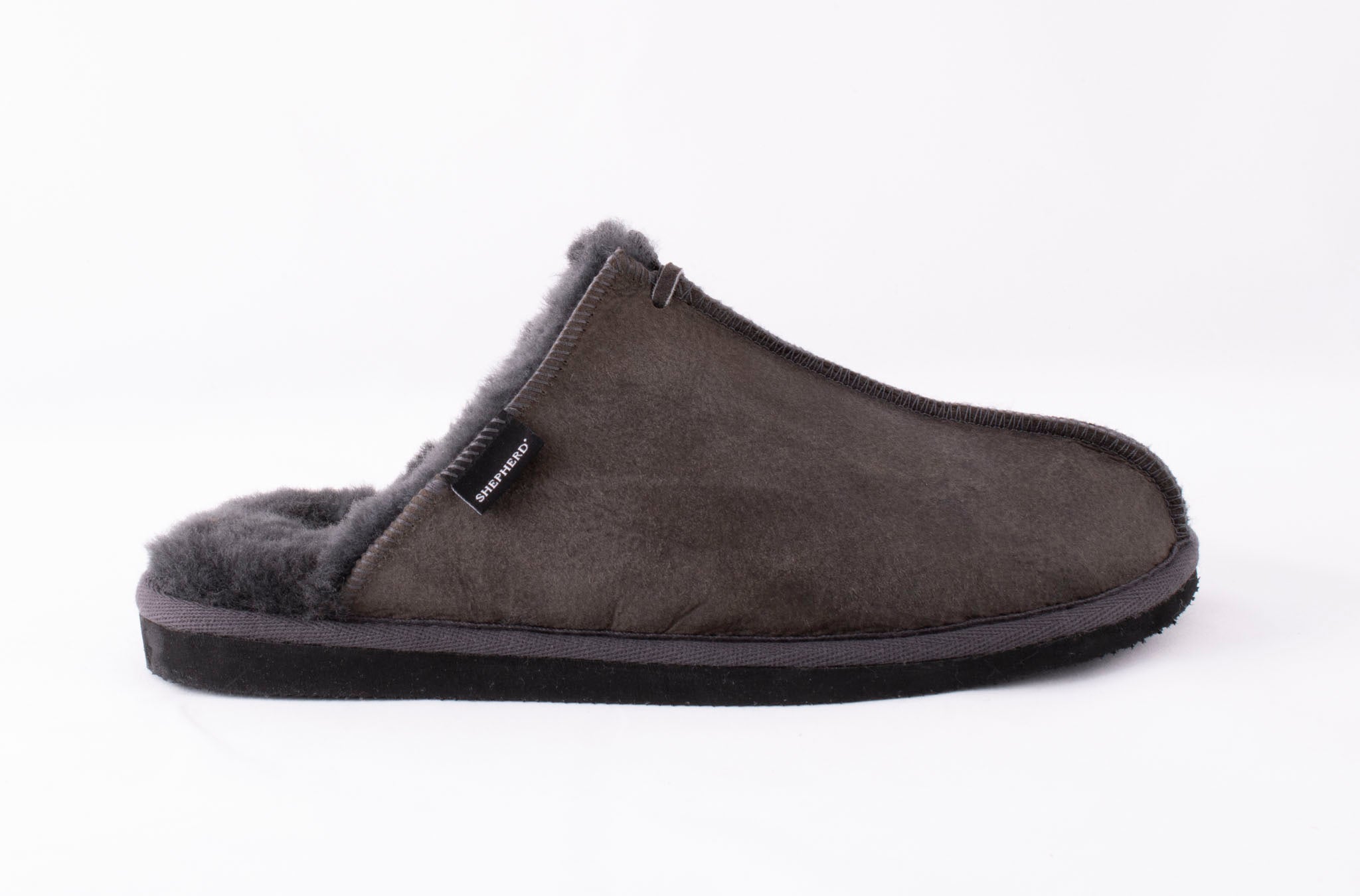 The Hugo Men's Sheepskin Slipper by Shepherd of Sweden in Asphalt Grey features a fuzzy-lined, slip-in design with a black sole and side fabric tag, shown against a plain white background.