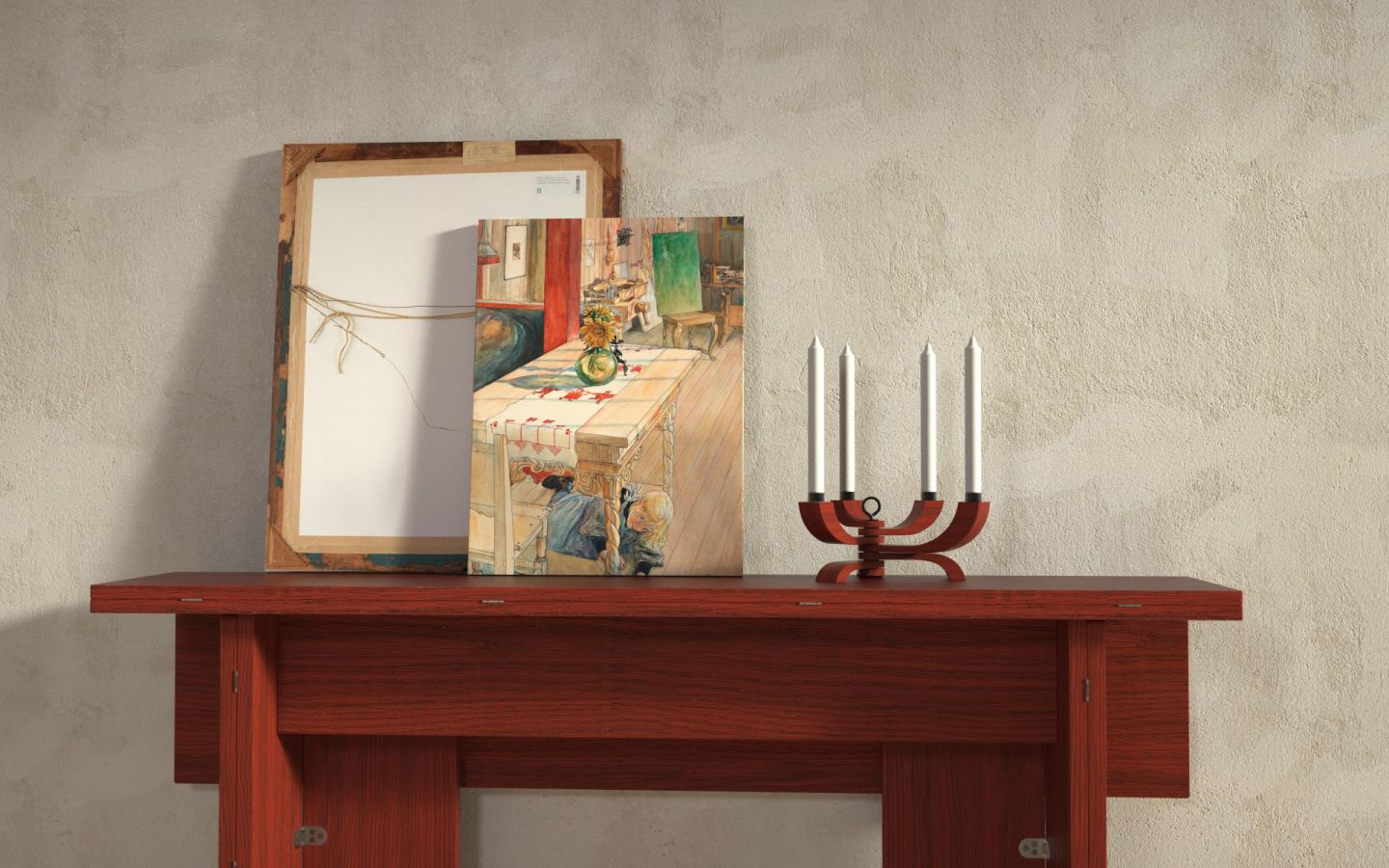 A red wooden console table holds two framed artworks—one showing a colorful room, the other backward—beside a Design House Stockholm Nordic Light Candle Holder 4 Arms in Red with four white candles, set against a light textured wall.